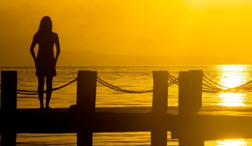 Image of a woman on a jetty with a sunset