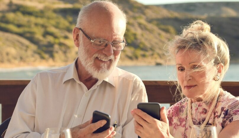 Two people sat on decking with phones and a beach behind them