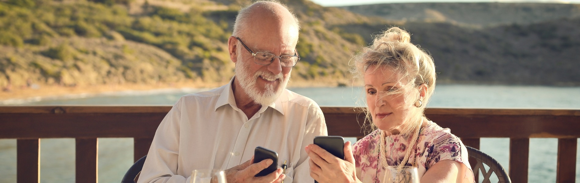 Two people sat on decking with phones and a beach behind them