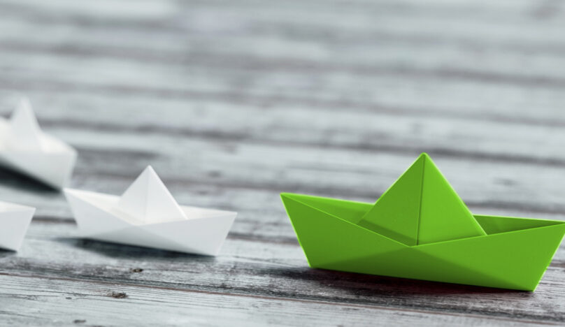 Positioning your brand as a thought leader - a green paper boat leads as other paper boats follow