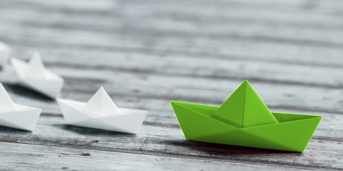 Positioning your brand as a thought leader - a green paper boat leads as other paper boats follow